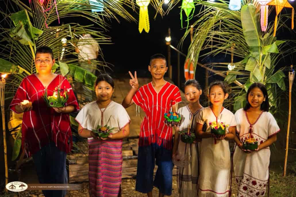 Children in traditional dress holding krathong under a lantern arch at night during Loy Krathong at The Bush Camp Chiang Mai