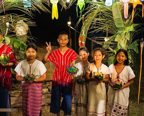 Children in traditional dress holding krathong under a lantern arch at night during Loy Krathong at The Bush Camp Chiang Mai
