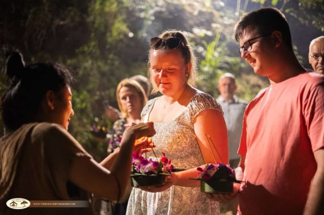 Guests holding orchid krathong while a team member lights the incense at The Bush Camp Chiang Mai Loy Krathong evening